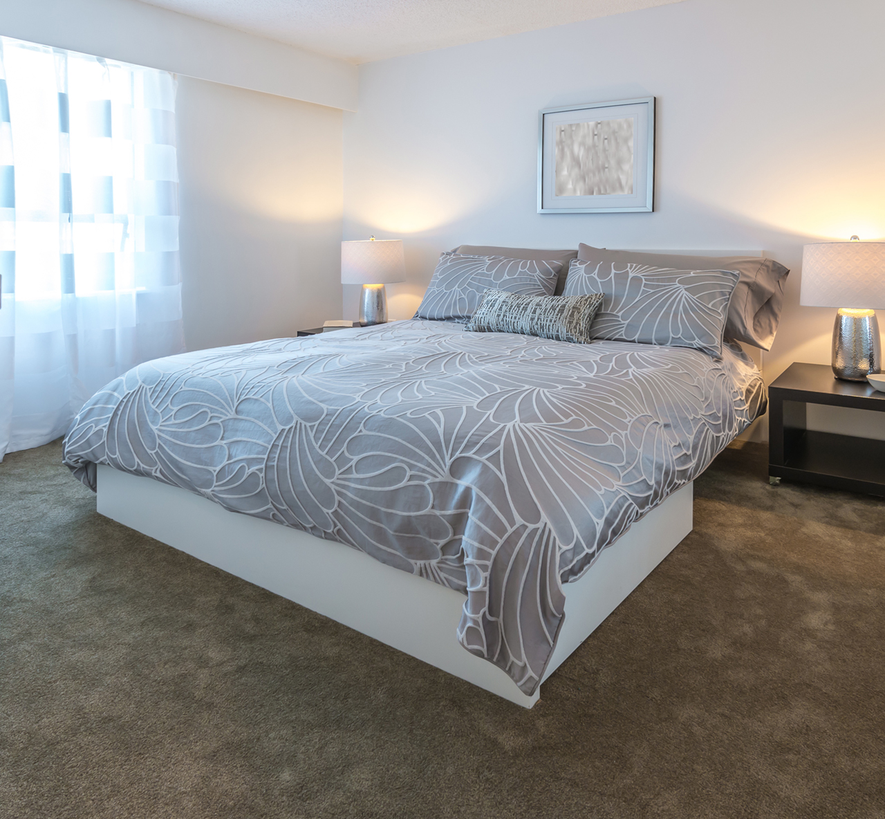 Interior bedroom view of a nice queen size bed with grey sheets near a window
